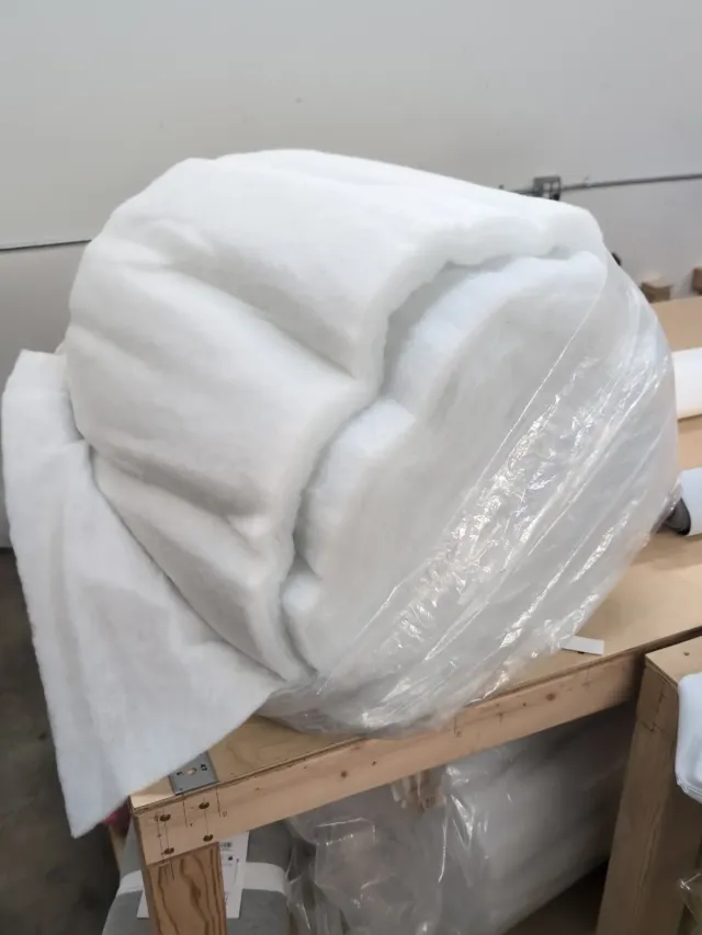 A large roll of white batting in a clear wrap on a workshop bench.