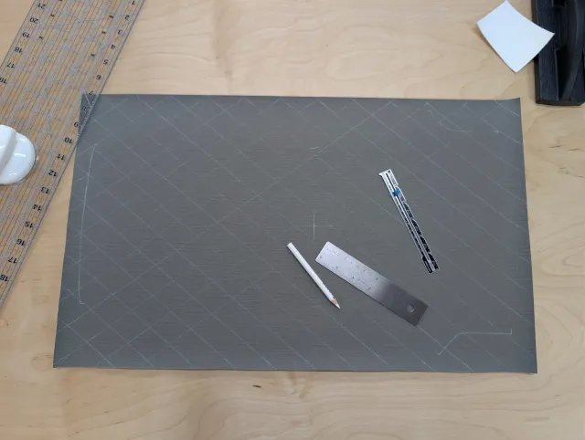 A charcoal fabric panel chalked with a diamond grid, with rulers and a chalk pencil on the bench.