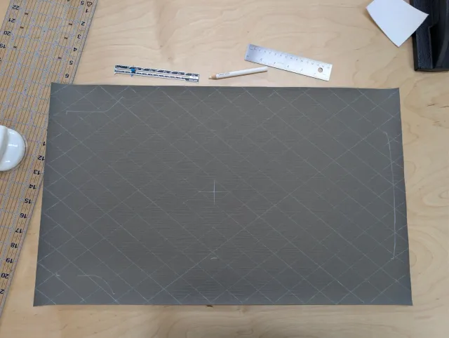 A charcoal panel chalked with a diamond grid and centre mark, rulers above it on the bench.