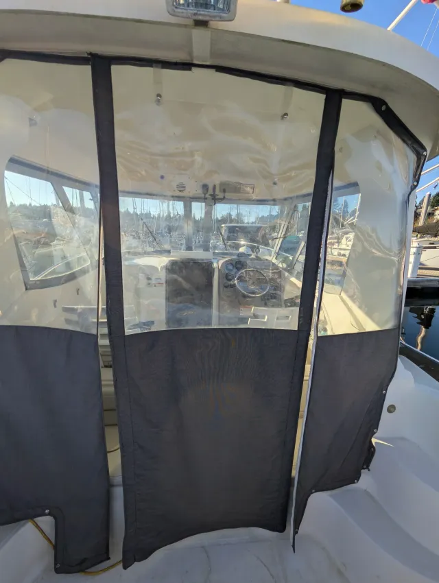 The original aft enclosure on the boat, dark lower curtains and clear windows hanging at the cockpit, marina beyond.