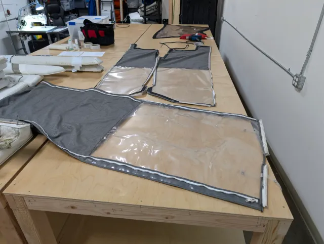 The old enclosure curtain sections laid out on the bench, grey fabric with clear vinyl windows and zippers.