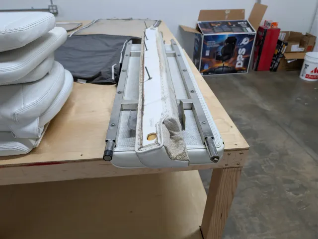 An old white vinyl seat bottom on its stainless frame, with a stack of white cushions beside it.