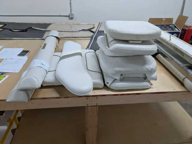 Old white vinyl cushions and bolsters stacked and laid out on the workshop bench.