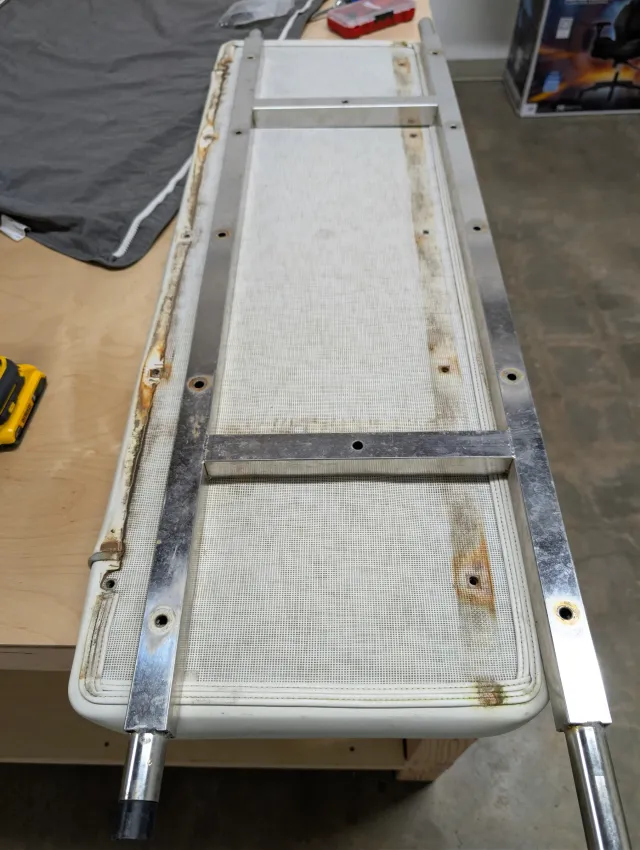 Underside of an old seat bottom: white mesh back on a stainless frame, with rust staining along the edges.