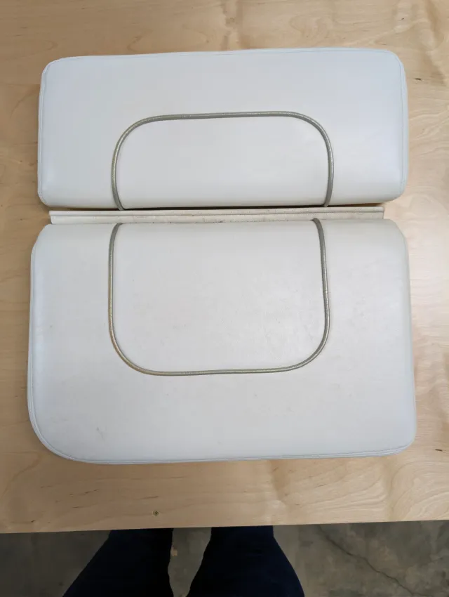 Two old white cushions with grey welt piping laid side by side on the bench.