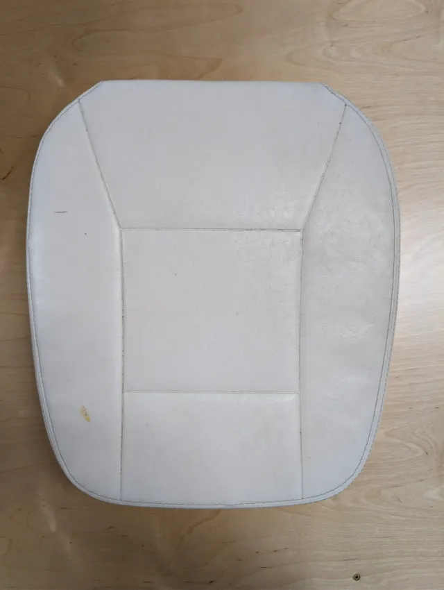An old white vinyl seat cushion, top side up on the bench, its panels marked and soiled.