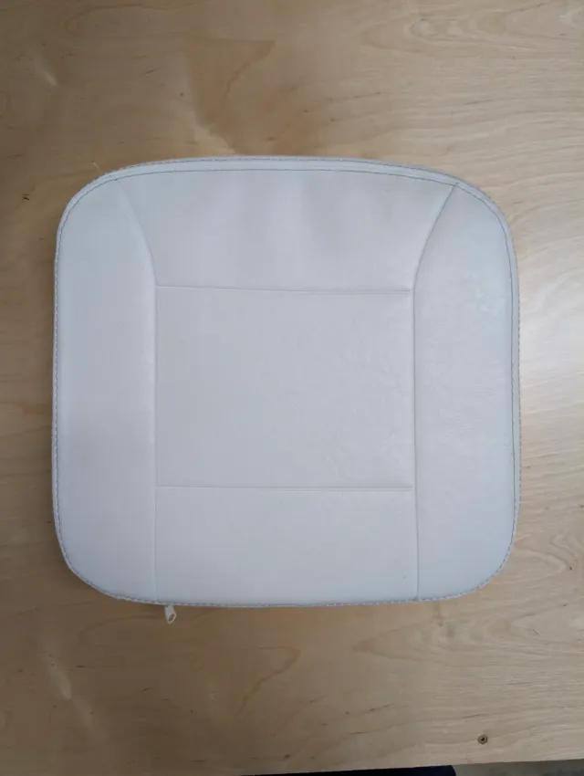 An old white seat cushion, square with rounded corners, a zipper pull at its lower edge.