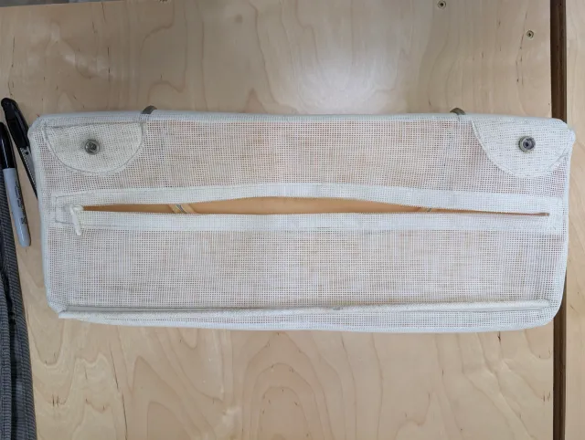 Back of an old cushion: a white mesh panel with a zipper pocket and two snap tabs.