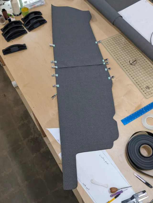 A charcoal curtain panel clipped together on the bench, with rulers, tapes and tools around it.