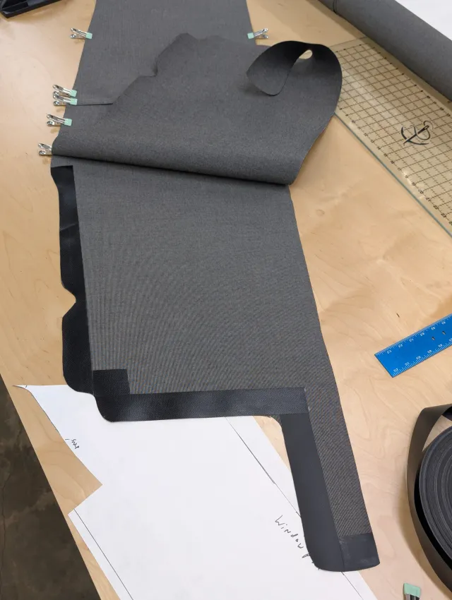 Charcoal curtain fabric with black edge banding on its corners and edges, pattern paper beneath.