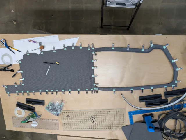 A curtain panel with a window opening, clipped all around, with clips and tools scattered on the bench.