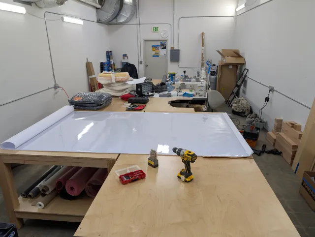 The workshop with a large sheet of clear vinyl rolled out on the bench and a drill in front.