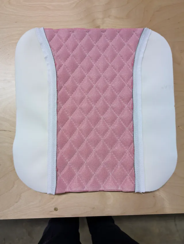 The reverse of a seat panel, pink foam backing under the quilting and white tape along the seams.