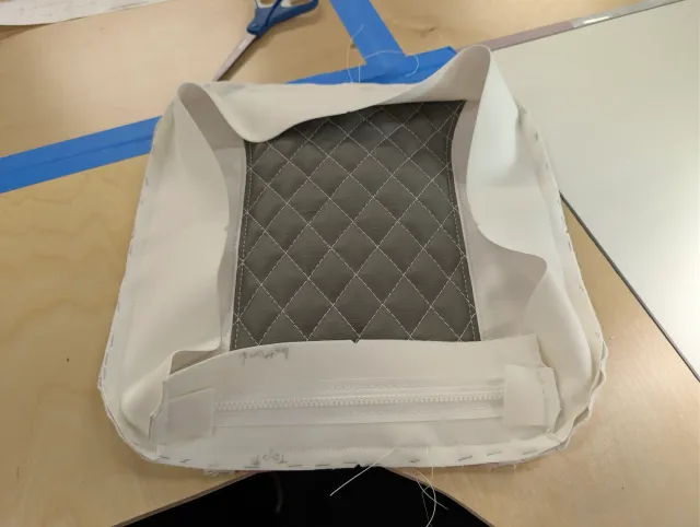 A cushion cover inside out, quilted panel visible, a zipper strip with tabs sewn into the boxing.