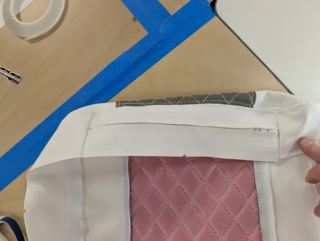 Inside of a cover, a hand holding the zipper placket above taped seams and pink quilted backing.