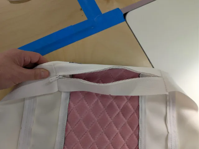 A hand pulling open the zipper in a cover's boxing, pink quilted backing visible inside.