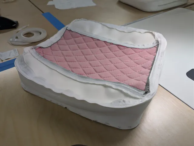 A seat cover inside out on a cushion, pink quilted backing visible, white boxing around the side.