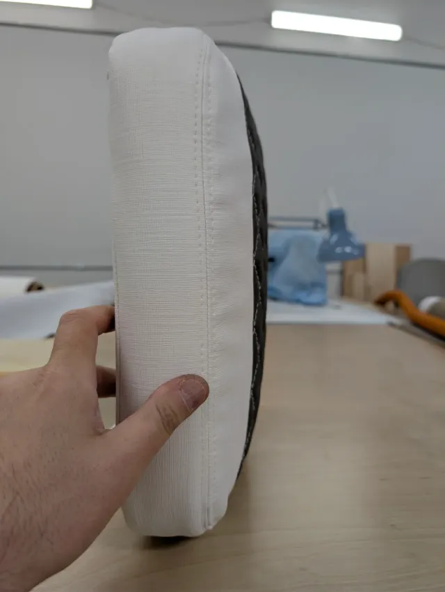 A hand holding a new cushion on edge, showing its smooth white boxing and seam.