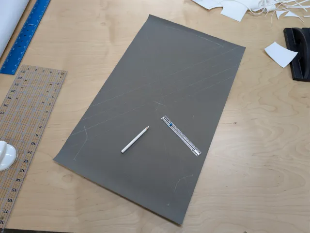 A charcoal fabric panel chalked with long diagonal lines and corner marks, a pencil and ruler on it.
