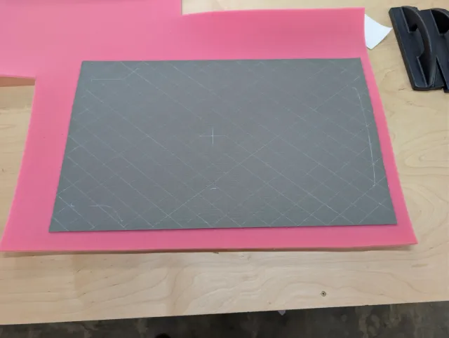 A charcoal panel with a diamond grid laid on a sheet of pink foam.