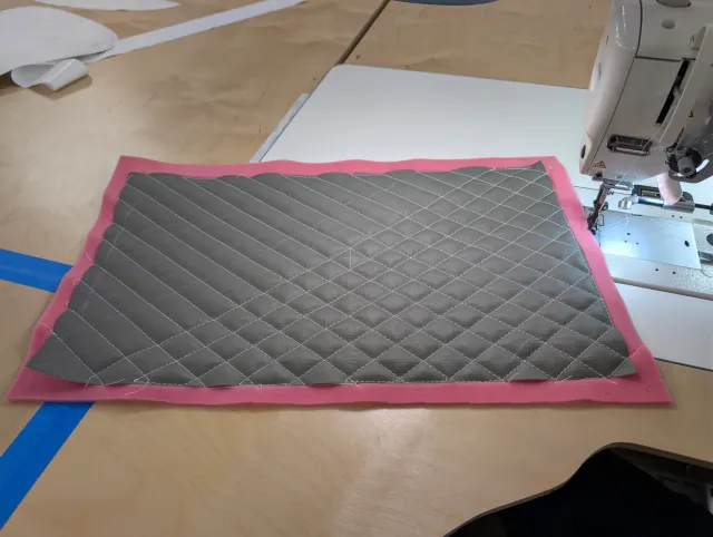 A quilted charcoal panel on pink foam beside the sewing machine.