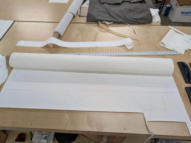 A roll of white fabric on pattern paper, with long pattern strips on the bench.