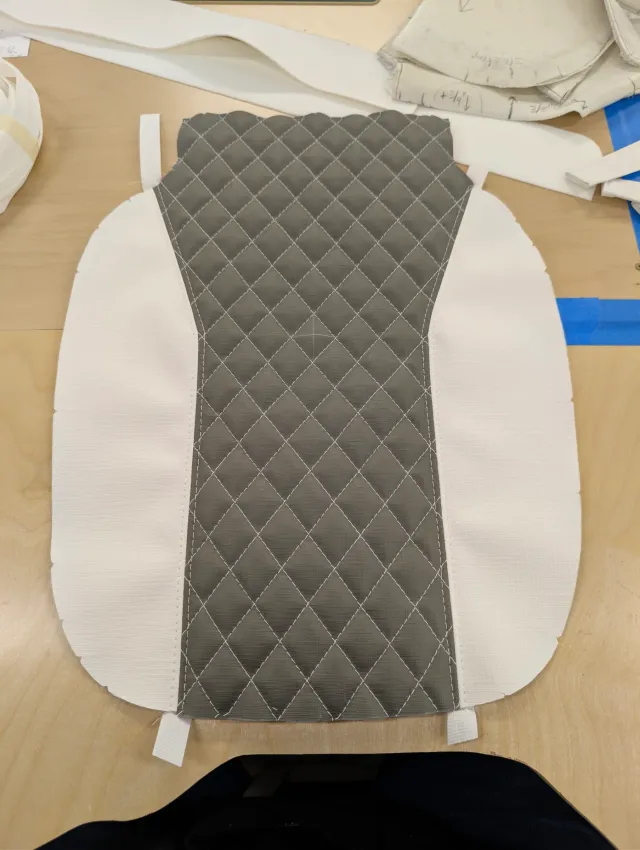A cushion top panel with a charcoal quilted centre between white sides, small tabs at its edges.