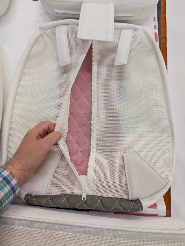 A hand opening the zipper in the mesh back of a seat bottom, pink quilted backing inside.