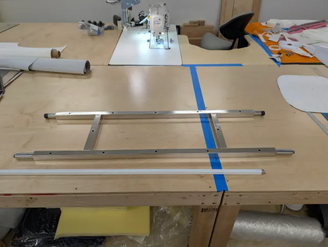 A polished stainless seat frame laid on the bench beside a long white track strip.