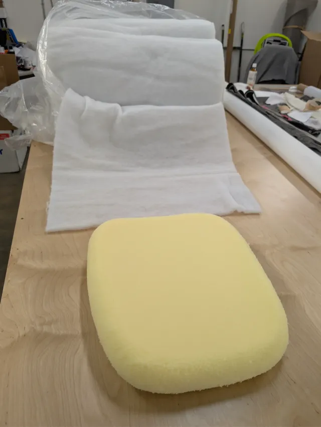 A block of yellow foam on the bench in front of a roll of white batting.