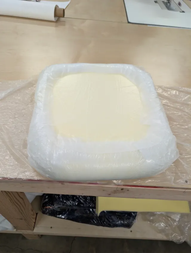 A foam cushion insert wrapped in clear plastic film, white batting around its edges.