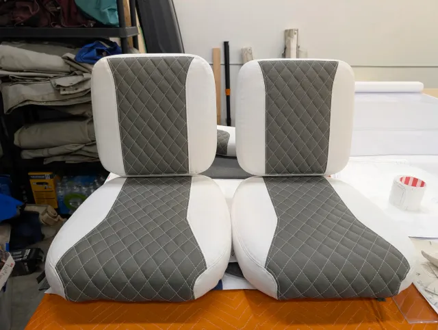 Two new seat bottoms with their backs standing on them, side by side, charcoal quilted centres on white.