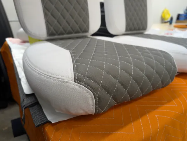 Close-up of a seat bottom corner, charcoal quilted top, white side and stitched edge.