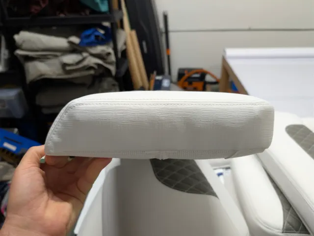 A hand holding a new bolster on edge, showing its white boxing and seam.