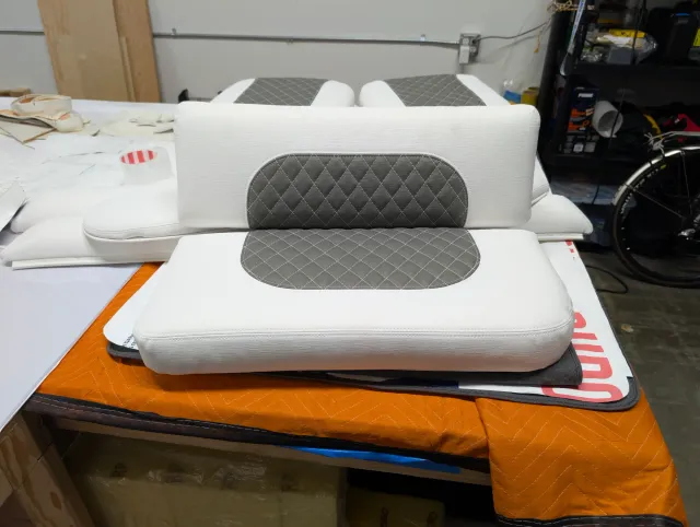 A bolster standing behind a seat bottom, both with oval charcoal quilted panels, on a moving blanket.