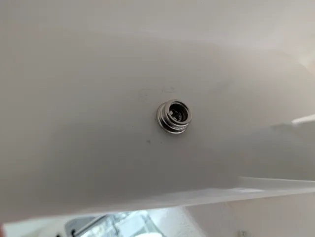 A snap stud fastened into a white fibreglass surface.
