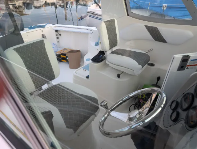 A view through the enclosure glass of two helm seats and a wall bolster, charcoal diamond quilting on white.