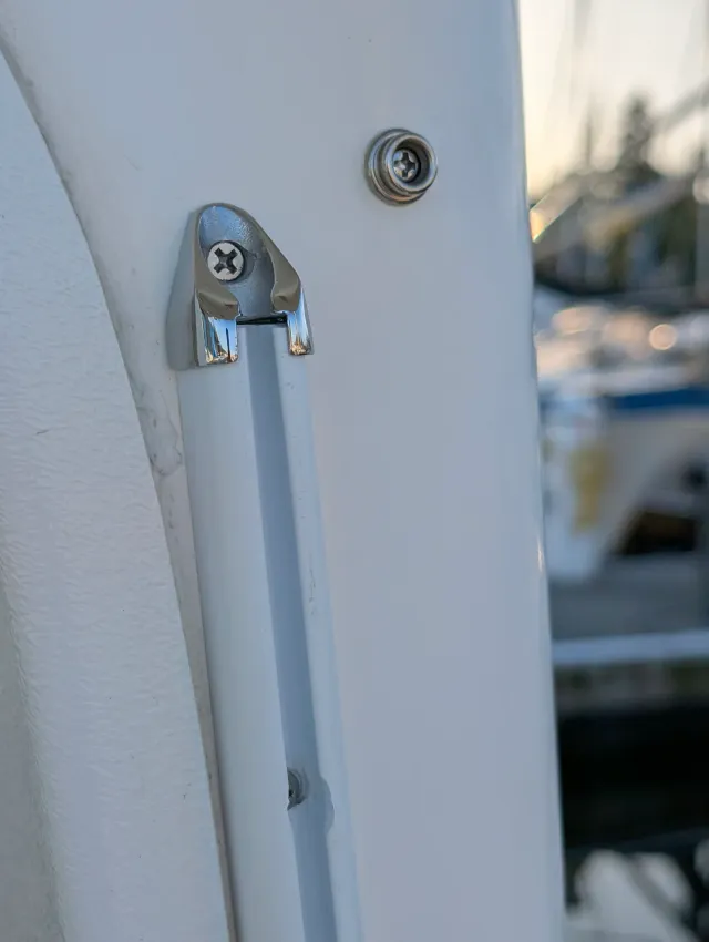 A stainless track end cap screwed to a white post, with a snap stud beside it.
