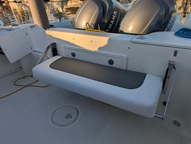 The aft fold-down seat lowered at the stern, white with a charcoal panel, twin outboards behind.
