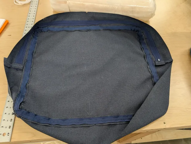 A cushion cover inside out on the bench, its zipper sewn into the boxing panel and fabric tape reinforced French seams visible.