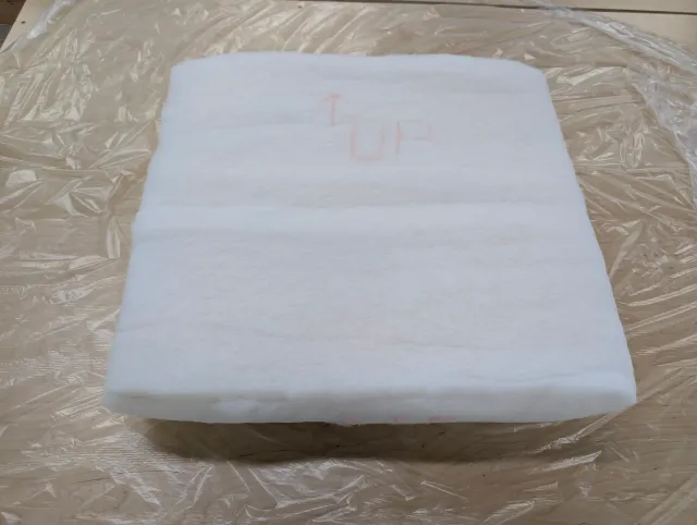 A cushion foam insert wrapped in white Dacron batting, marked UP, on a sheet of film.