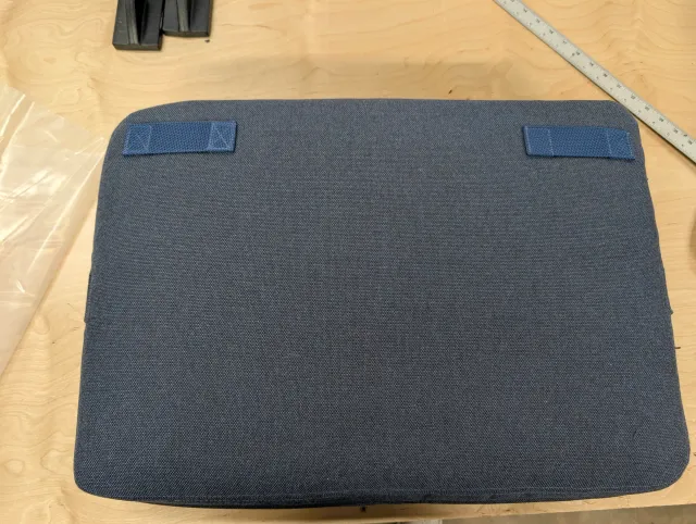 The back face of a back cushion with two navy webbing tabs sewn on for its straps.