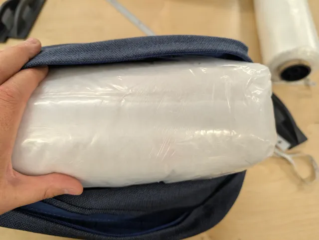 A film-wrapped foam insert being slid into its cover through the open zipper.