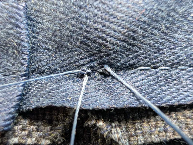 A needle and thread closing the last of a seam by hand, close up on navy fabric.