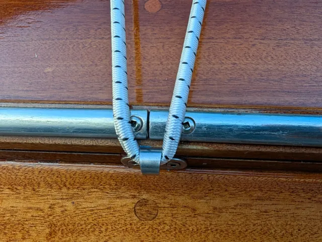 Shock cord passing through a 316 stainless steel lashing hook on the teak rail.