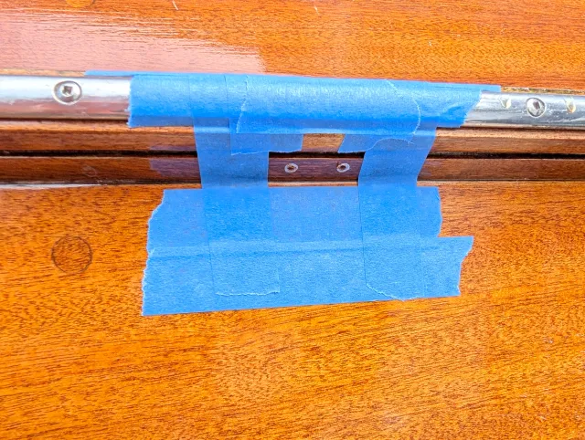 Blue tape masking the varnished wood beside the rail where a fitting is to be mounted.