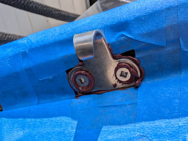 Close-up of the new stainless hook plate bedded in sealant on the masked rail.
