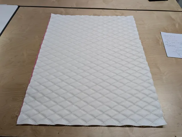 A flat panel of white marine vinyl quilted in a double diamond pattern on the workbench.