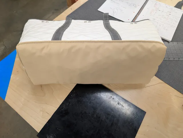 The tote lying on its side showing the tan bottom panel with a welted edge, and the strap ends at the top.