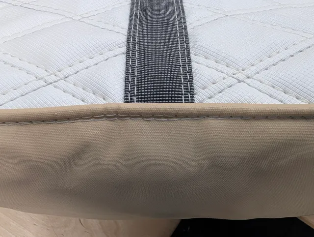 Close-up of a grey strap meeting the tan welted bottom panel, with rows of cream stitching.